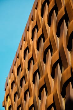 A stunning and captivating architectural facade featuring a unique woven design in warm tones set against a vibrant sky