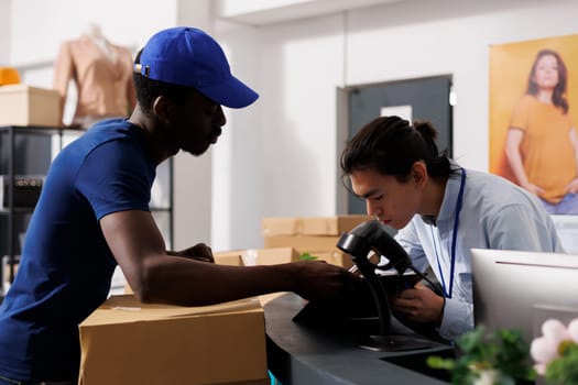 Store worker signing delivery files, discussing packages details with manager in clothing store. African american courier preparing to ship customers online orders, explaining logistics to employee