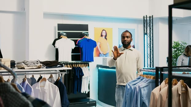 African american shopper using hologram in boutique to check new clothing store merchandise with augmented reality. Male customer looking at holographic footage, artificial intelligence.