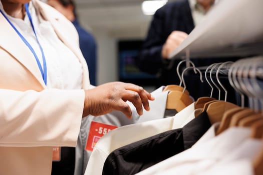 Retail clothing store worker doing merchandising, restocking empty racks during seasonal sales, close up. Shop sales assistant displaying and organizing clothes in fashion outlet