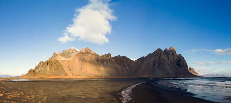 Panoramic view of vestrahorn rocky hills on icelandic peninsula, with unique black sand beach and nordic outdoor setting. Incredible landscape created by mountain top and ocean waves.
