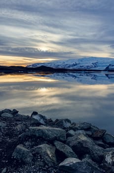 Scandinavian frosty lake near highlands forming nordic winter landscape at sunset, large body of water and snowy mountains in icelandic scenery. Frozen fields in spectacular countryside.