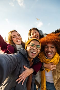 Selfie portrait of multiracial happy friends enjoying sunny winter day outdoors. Group of people looking at camera smiling. Vertical image. Copy space. Lifestyle concept.