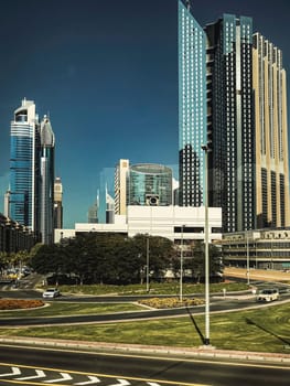A photo of a modern city skyline with tall glass buildings and a curved highway in the foreground. The image has a vintage feel and a blue sky with clouds. High quality photo