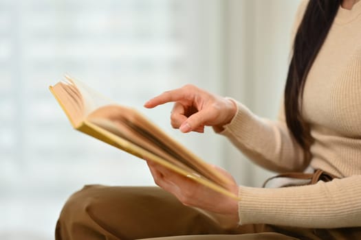 Cropped image of young woman in casual clothes reading book at home. People, leisure and lifestyle concept.