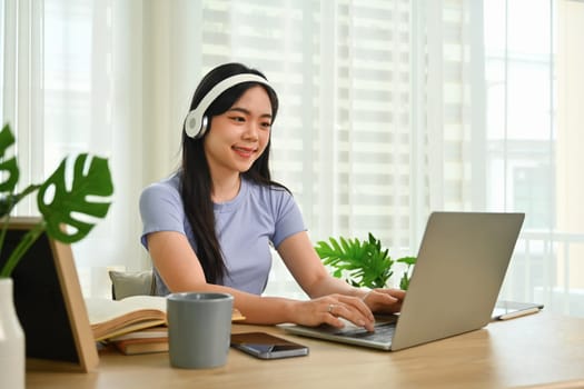 Pretty young woman wearing wireless headphone learning distantly, watching online lecture on laptop screen.