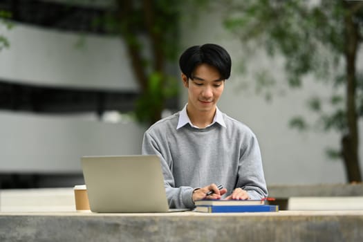 Smiling asian male student reading books, preparing for exam on table at campus. Youth lifestyle and education concept.