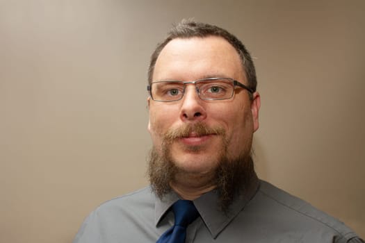 A man with a beard and glasses is wearing a blue tie. He is smiling and looking at the camera