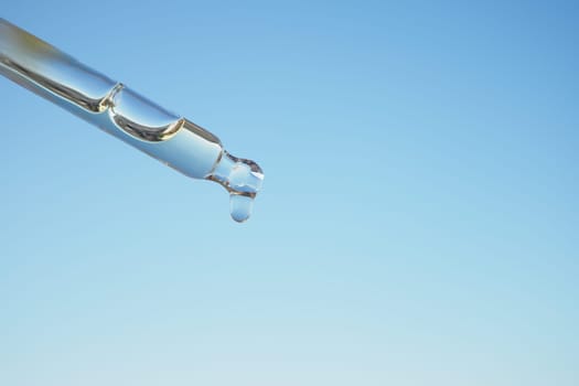 A single droplet gracefully hangs from a pipette set against a calm, serene blue backdrop
