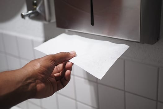 A hand reaches out and takes a paper towel from a tidy dispenser located in a clean restroom