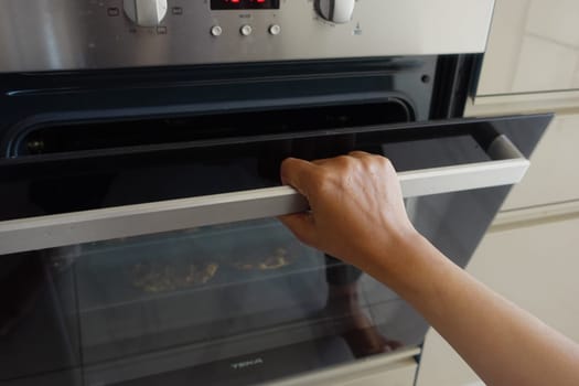 A hand is firmly grasping the handle of the oven door in order to open it properly