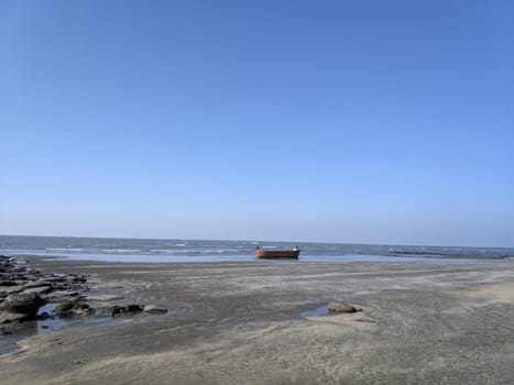 A lone boat sits on a shallow, rocky shoreline with the vast ocean and clear blue sky in the background.
