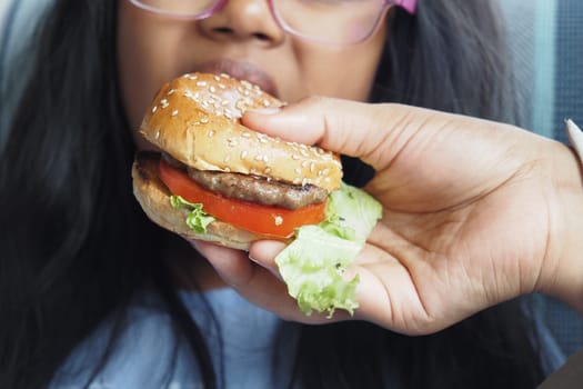 A hand offers a delicious and mouthwatering burger to a very hungry child waiting eagerly