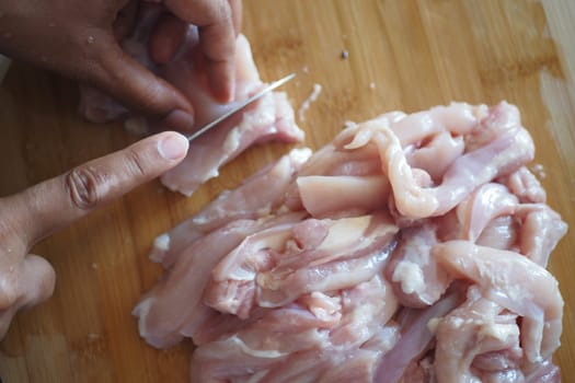 A skilled hand expertly cuts raw chicken into precise strips for meal preparation purposes