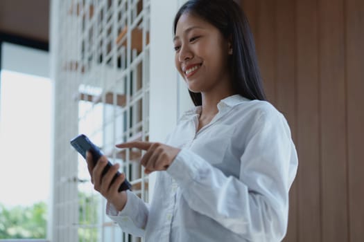 A young woman enjoys a moment of connection with her smartphone indoors, smiling as she interacts with technology and embraces modern lifestyle trends.