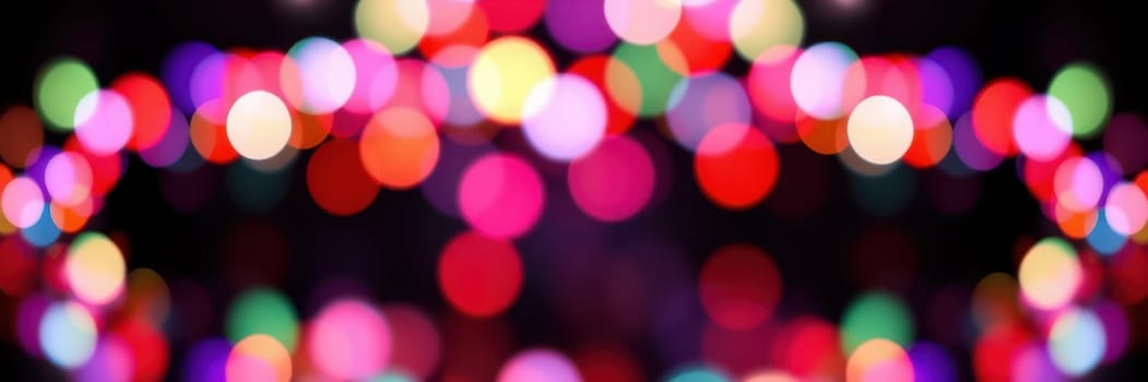 Colorful bokeh lights illuminate the night sky during a festive outdoor gathering, filling the park with a cheerful ambiance as people mingle and celebrate.