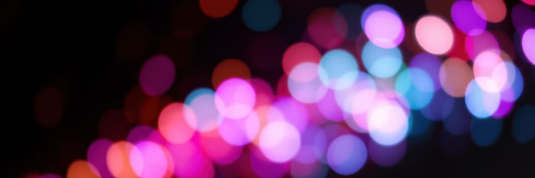 A collection of multicolored, blurred lights creates a festive ambiance in a bustling city during an evening event. The bright hues indicate a lively atmosphere.