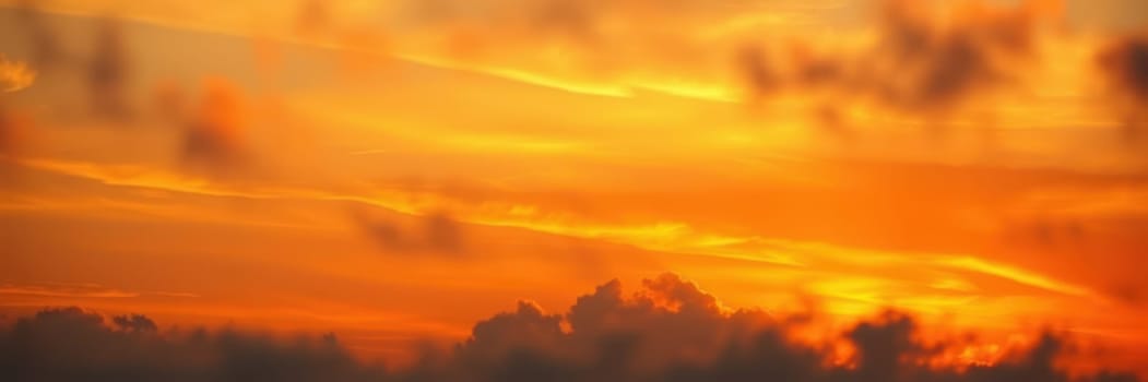 A stunning sunset spreads warm tones of orange and yellow across the sky, with clouds gently illuminated and silhouetted against the vibrant horizon during evening hours.