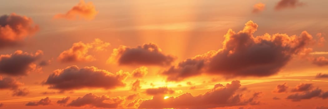 Bright orange and gold hues fill the sky as the sun rises above the horizon, casting a warm glow over the tranquil ocean waters and fluffy clouds floating peacefully.