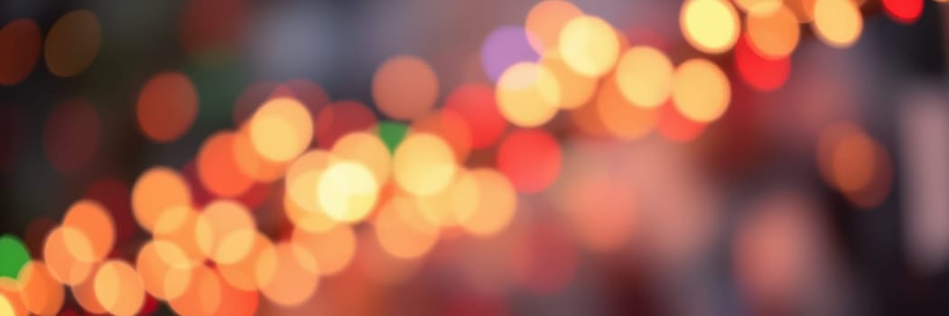 Bright, colorful lights illuminate the busy streets during an evening celebration. The soft glow creates a warm and inviting atmosphere as people gather to enjoy the festivities.