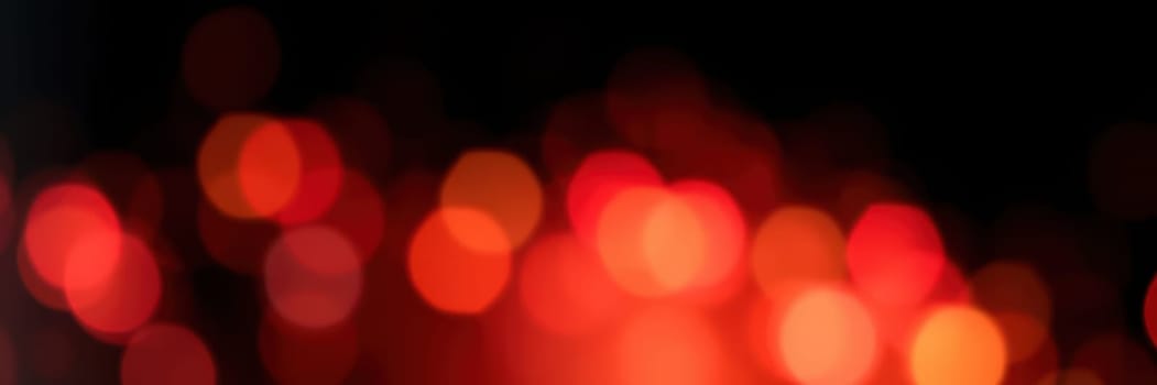 Warm red and orange lights twinkle softly in a blurred background, creating a cozy ambiance. The vibrant colors evoke feelings of joy during a nighttime celebration.