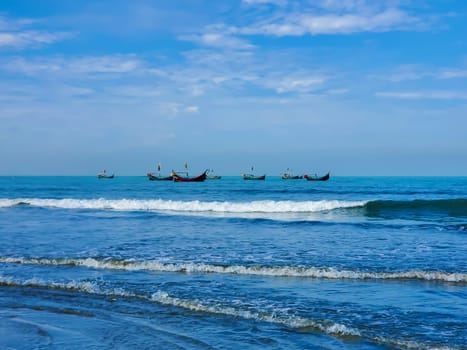 The image shows several small boats fishing in the ocean near the shoreline, with gentle waves and a clear blue sky overhead.