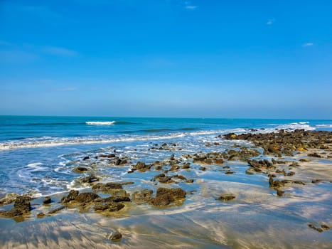Rocky beach with waves washing around stones under a clear blue sky.