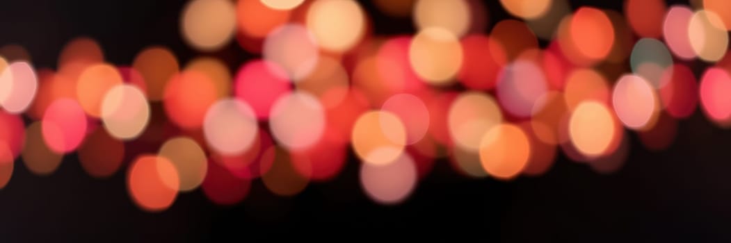 Colorful bokeh lights twinkle softly in a blurred background, enhancing the cozy and celebratory mood of an evening event. The vibrant hues of red and orange illuminate the surroundings.