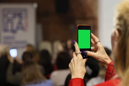 An individual is capturing a lively event scene with a smartphone, featuring a bright and vibrant green screen