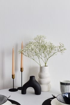 A sleek and modern tabletop arrangement showcasing an artistic vase, elegant candles, and delicate fresh flowers