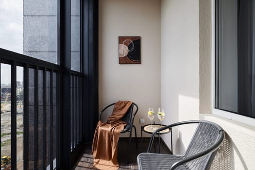 A stylish balcony with two elegant chairs, a cozy throw, and refreshing drinks creates a relaxing atmosphere