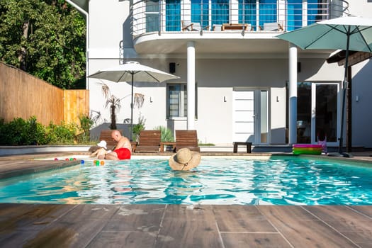 Family with young child enjoying a sunny day in the villa swimming pool, relaxing together. Concept of family bonding, leisure, and relaxation outdoors