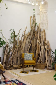 A stylish interior with a vibrant yellow chair, rustic logs, and lush greenery, giving a perfect bohemian vibe