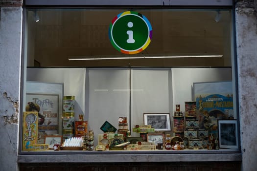 Cremona, Italy - November 27th 2024 Shop window in cremona, italy, showcasing local products and vintage advertising posters, with a prominent tourist information sign