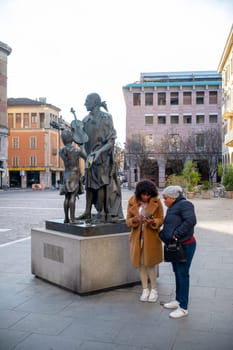 Cremona, Italy - November 27th 2024 Two tourists are using a smartphone near the monument to antonio stradivari, the famous violin maker, in cremona, italy