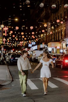 A charming couple leisurely strolls through a bustling city street, which is beautifully adorned with vibrant lanterns