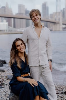 A fashionable couple joyfully shares a moment by the picturesque water, with a breathtaking city skyline behind them. Brooklyn bride and Manhattan in New York.