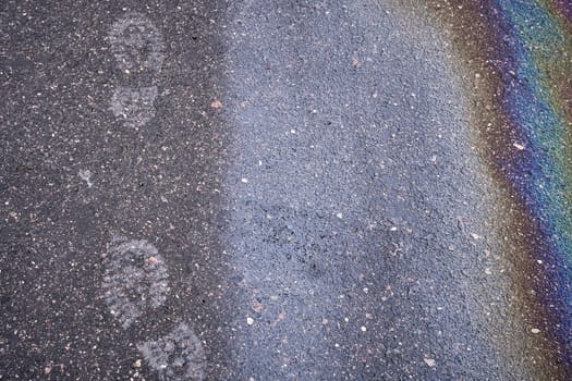 Wet asphalt with footprints and rainbow colors creates a unique and colorful textured background.