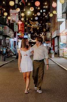 A couple enjoys a lovely stroll, hand in hand, beneath the colorful lanterns adorning the vibrant city streets