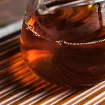 A closeup of warm amber liquid in a glass on a rustic table evokes feelings of comfort and serenity