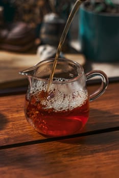 A vibrant tea being poured into a glass jug, showcasing rich colors and texture on a wooden surface.