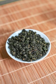 Closeup of dried green tea leaves arranged in a bowl, showcasing their vibrant color and intricate texture