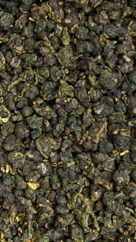 This is a detailed closeup view of dried green tea leaves, showcasing their unique texture and vibrant color