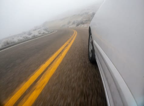 A car is driving down a road with yellow lines. The road is wet and the car is going fast