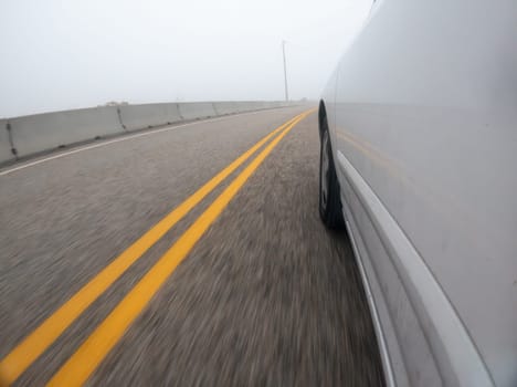 A car is driving down a road with yellow lines. The car is white and is in the middle of the road