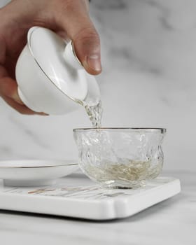 A gentle hand expertly pours steaming tea from a classic white teapot into a beautifully crafted glass cup