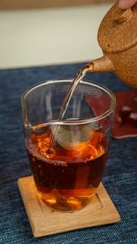 A serene moment of tea carefully being poured into a delicate glass cup that rests on a smooth wooden coaster
