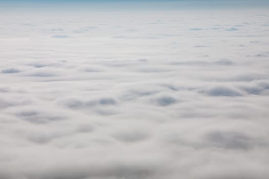 A vast expanse of low-lying clouds blankets the landscape. The view, likely from an airplane, shows a dense layer of fog or stratus clouds. No people are visible.