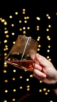 A hand holding a glass of rich liquor, surrounded by golden bokeh, creating a warm, inviting atmosphere