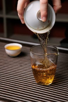 A hand pours fragrant tea from a ceramic cup into a glass, showcasing the art of tea preparation and enjoyment